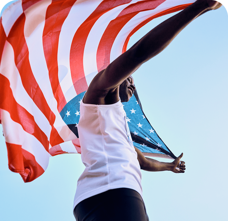 Athlete holding American flag, blue sky background.