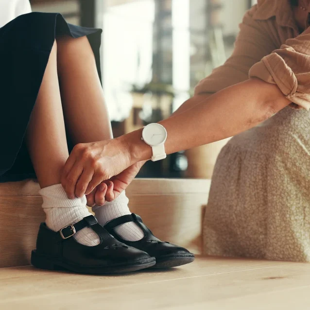 Adult helping child with black shoes.